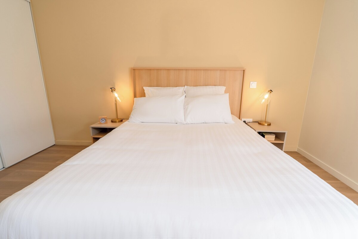 A neatly made bed with white linens, two bedside tables with lamps, and a wooden headboard.