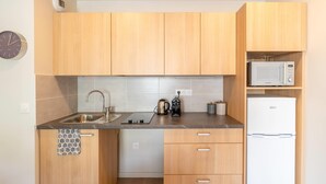 A modern kitchen with wooden cabinets, a stainless steel sink, a kettle, a microwave, and a refrigerator. - Quality Aparthotel Villefontaine (Villefontaine)