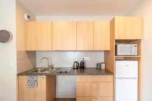 A modern kitchen with wooden cabinets, a stainless steel sink, a microwave, and a white refrigerator. - Quality Aparthotel Villefontaine (Villefontaine)