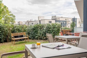 An outdoor patio area with a table, chairs, a bench, and a glass of orange juice. - Quality Aparthotel Villefontaine (Villefontaine)