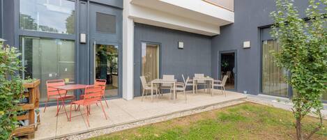 A modern building with a patio area featuring outdoor seating and a small garden.