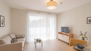 Una sala de estar moderna con un sofá, una mesa de centro, un televisor sobre un mueble de madera y un comedor con una mesa y sillas.