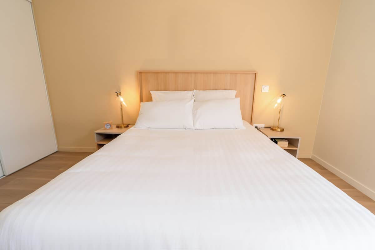 A neatly made bed with white linens, two bedside tables with lamps, and a wooden headboard.