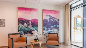 Una habitación con dos sillones naranja, una pequeña mesa redonda con un jarrón de flores blancas y dos grandes cuadros de paisajes en la pared.