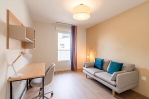 A modern, well-lit room with a desk, chair, and sofa. - Quality Aparthotel Villefontaine (Villefontaine)