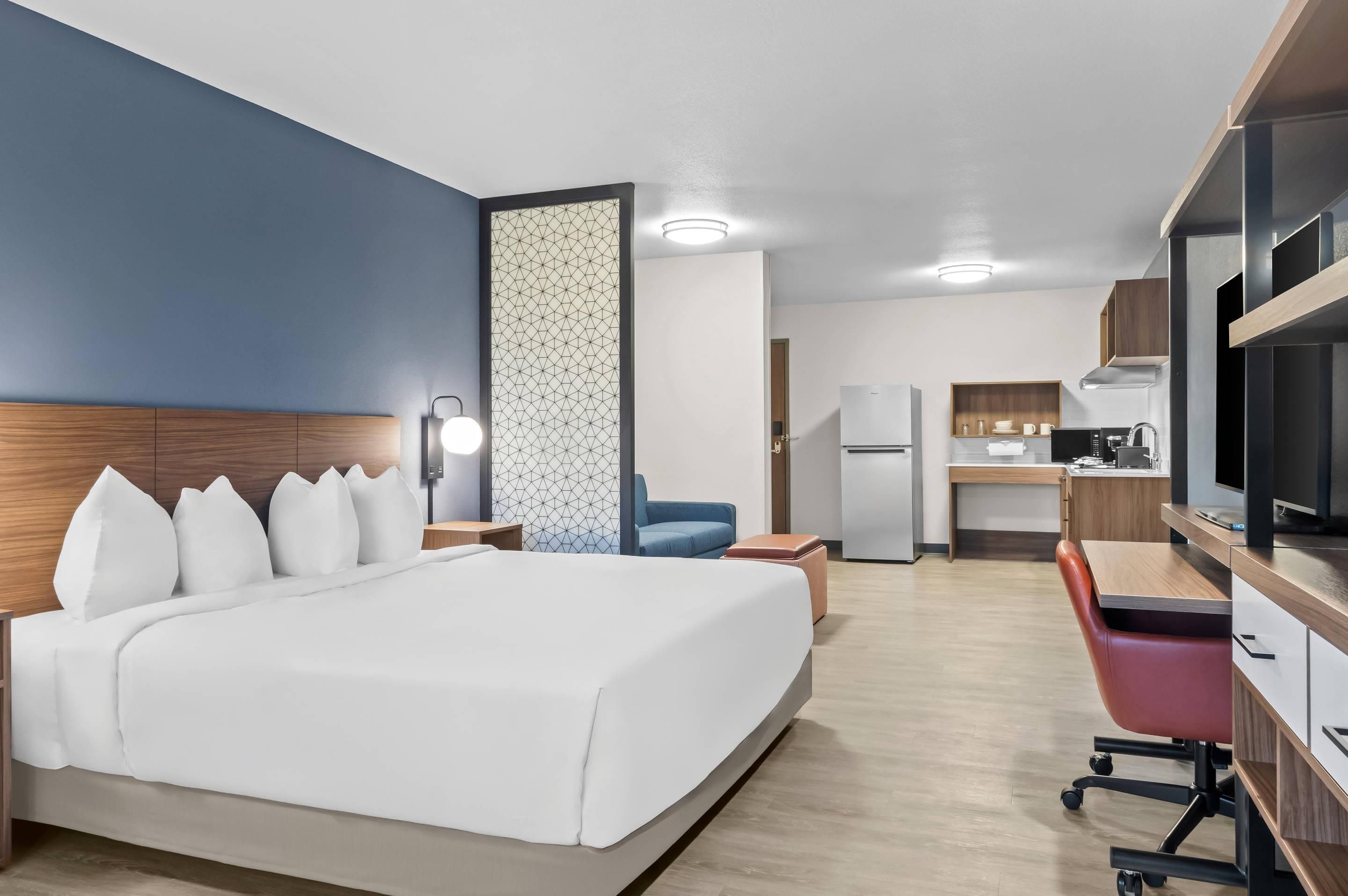 Une chambre d’hôtel équipée d’un lit, d’un bureau, d’une chaise, d’une télévision et d’une kitchenette.
