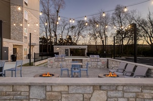 Un patio al aire libre con muros de piedra, una parrilla, fogones y luces colgantes.