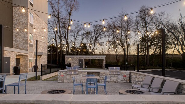Eine Terrasse im Freien mit Steinsitzgelegenheiten, Grillplatz und Lichterketten.