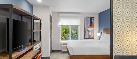 Una habitación de hotel moderna con una cama grande, televisión, escritorio y ventana con vistas a zonas verdes.