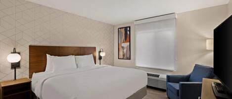 A hotel room with a large bed, a desk with a computer, a chair, a TV, and a painting on the wall.