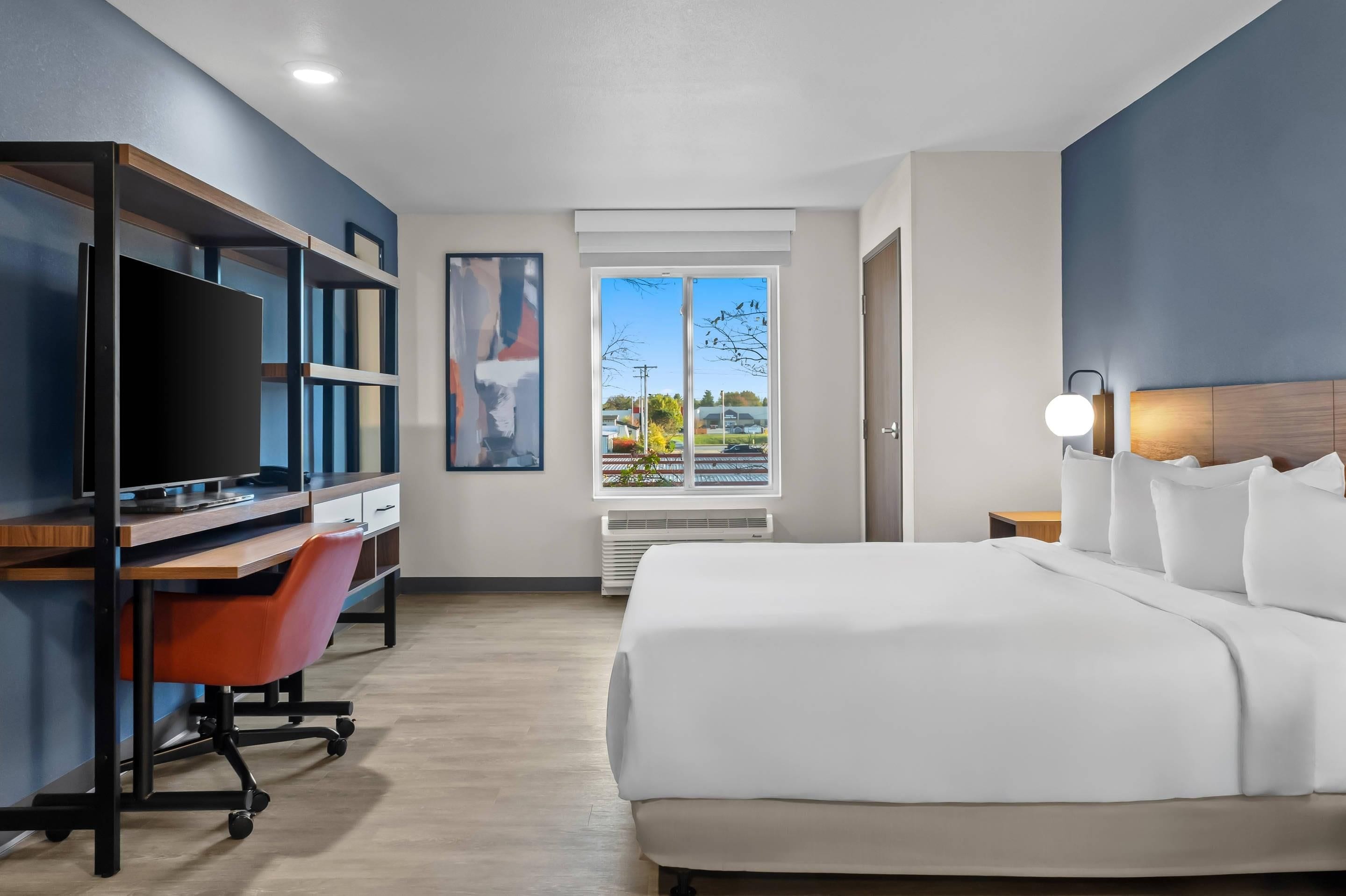 Een moderne hotelkamer met een groot bed, een bureau met een computer, een televisie en een raam met uitzicht.