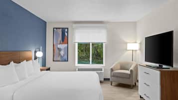 A hotel room with a large bed, a TV, a chair, and a window with a view of greenery.