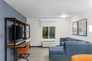 Una sala moderna con un televisor de pantalla plana, un escritorio de madera, un sofá azul y una ventana con vistas a zonas verdes.
