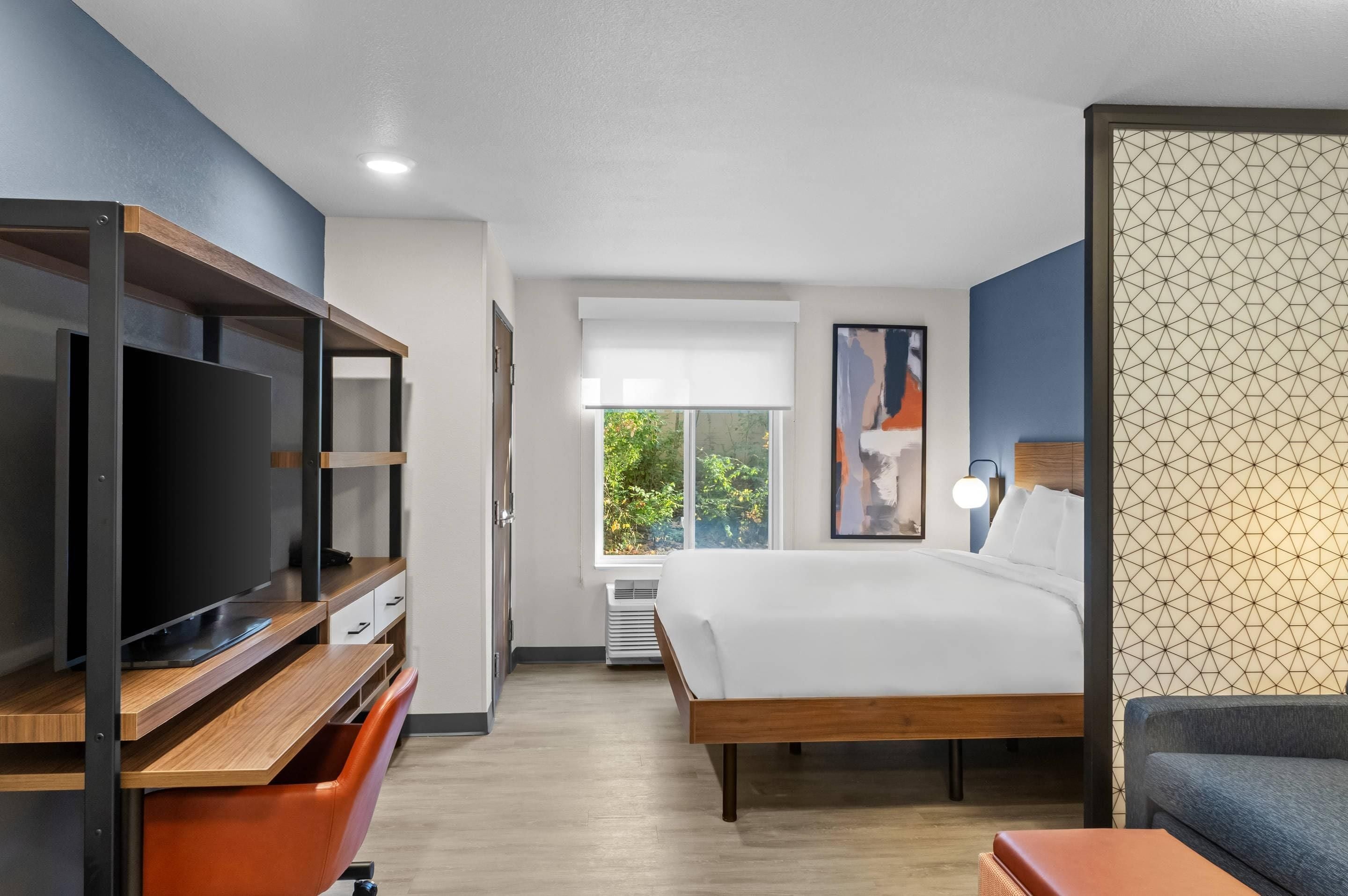 Een moderne hotelkamer met een groot bed, een televisie, een bureau en een raam met uitzicht op groen.