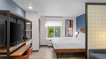 Een moderne hotelkamer met een groot bed, een televisie, een bureau en een raam met uitzicht op groen.