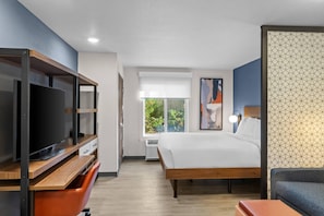 Een moderne hotelkamer met een groot bed, een televisie, een bureau en een raam met uitzicht op groen.