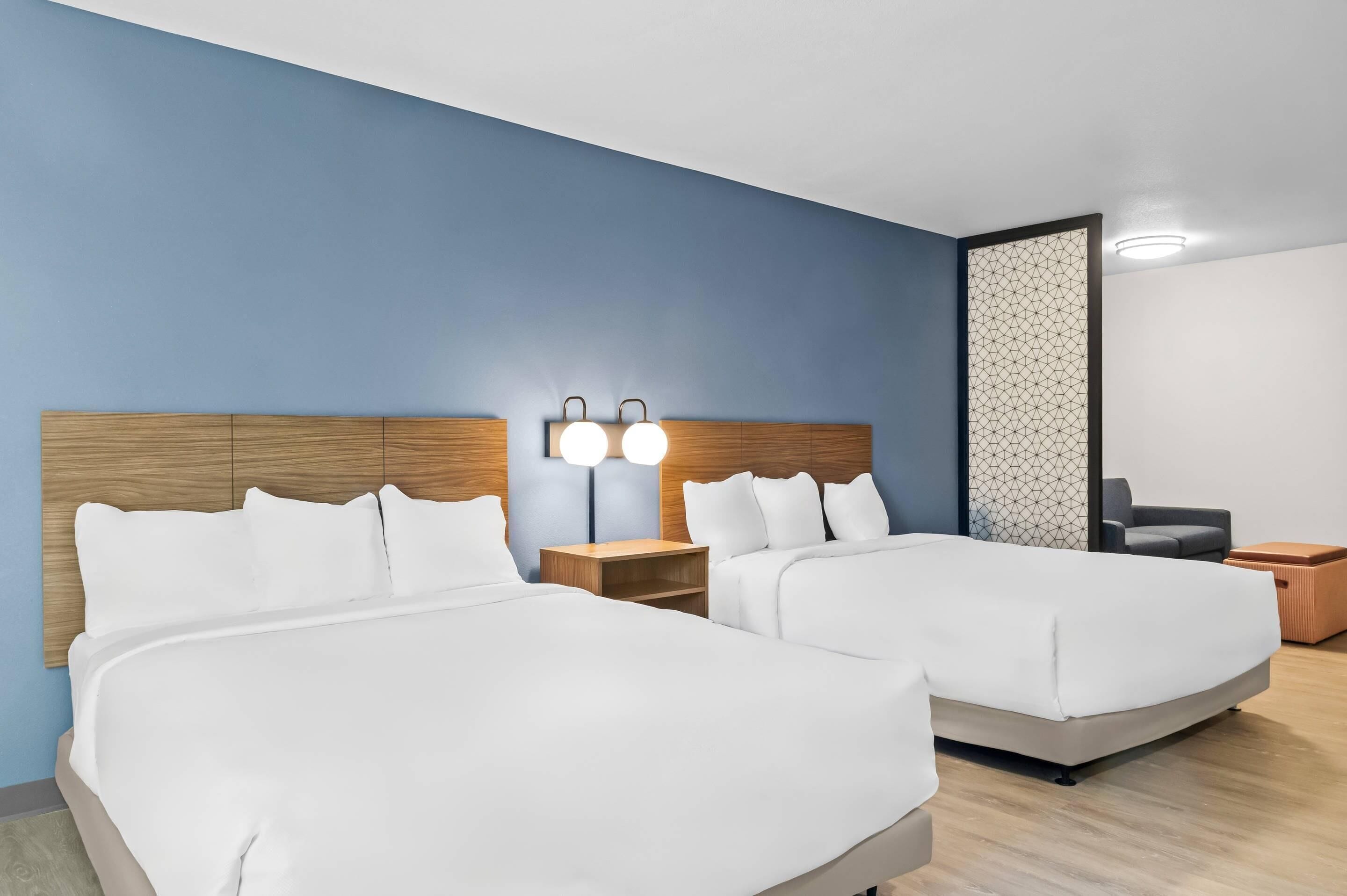 A hotel room with two beds, wooden headboards, bedside tables with lamps, and a geometric-patterned partition.