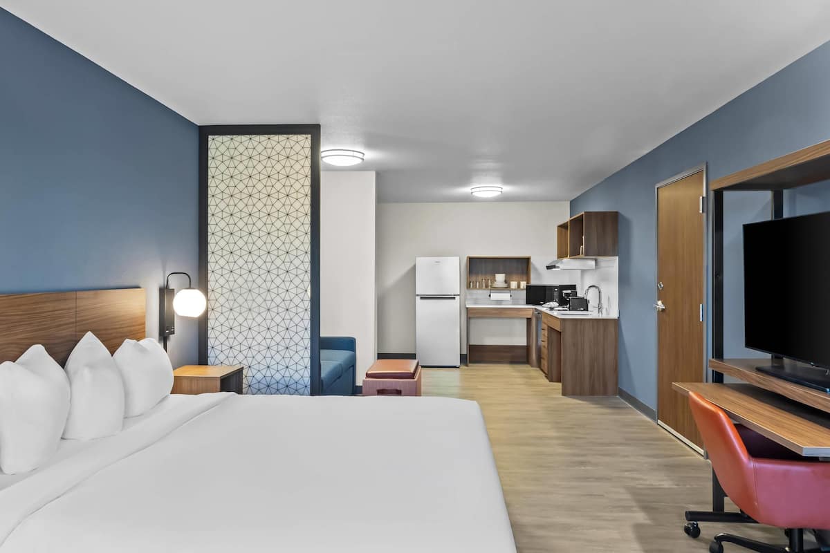 Ein Hotelzimmer mit Bett, Schreibtisch, Fernseher, einer Küchenzeile und einem Badezimmer.
