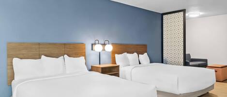 A hotel room with two beds, a nightstand with a lamp, a seating area with a chair, and a patterned wall.
