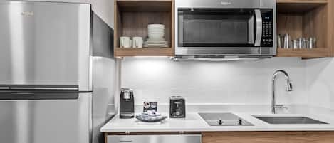 A modern kitchen with a stainless steel refrigerator, a microwave, a coffee maker, a toaster, and a dishwasher.