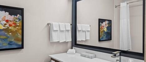 A modern bathroom with a white sink, a large mirror, and two towels hanging on the wall.