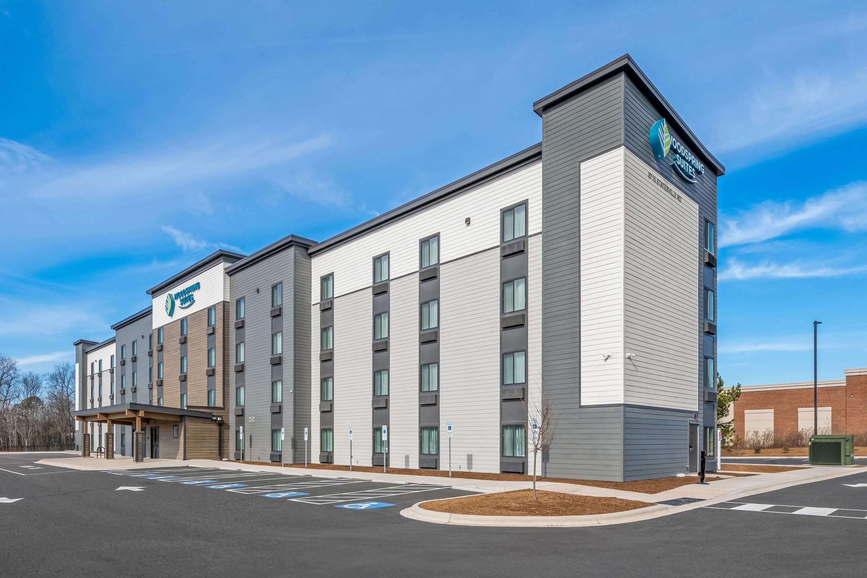 A modern hotel building with a flat roof, multiple windows, and a parking lot with marked spaces.