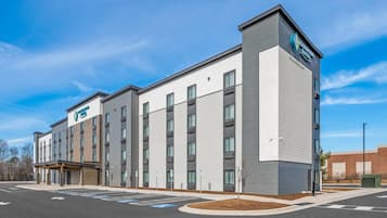 A modern hotel building with a flat roof, multiple windows, and a parking lot with marked spaces.