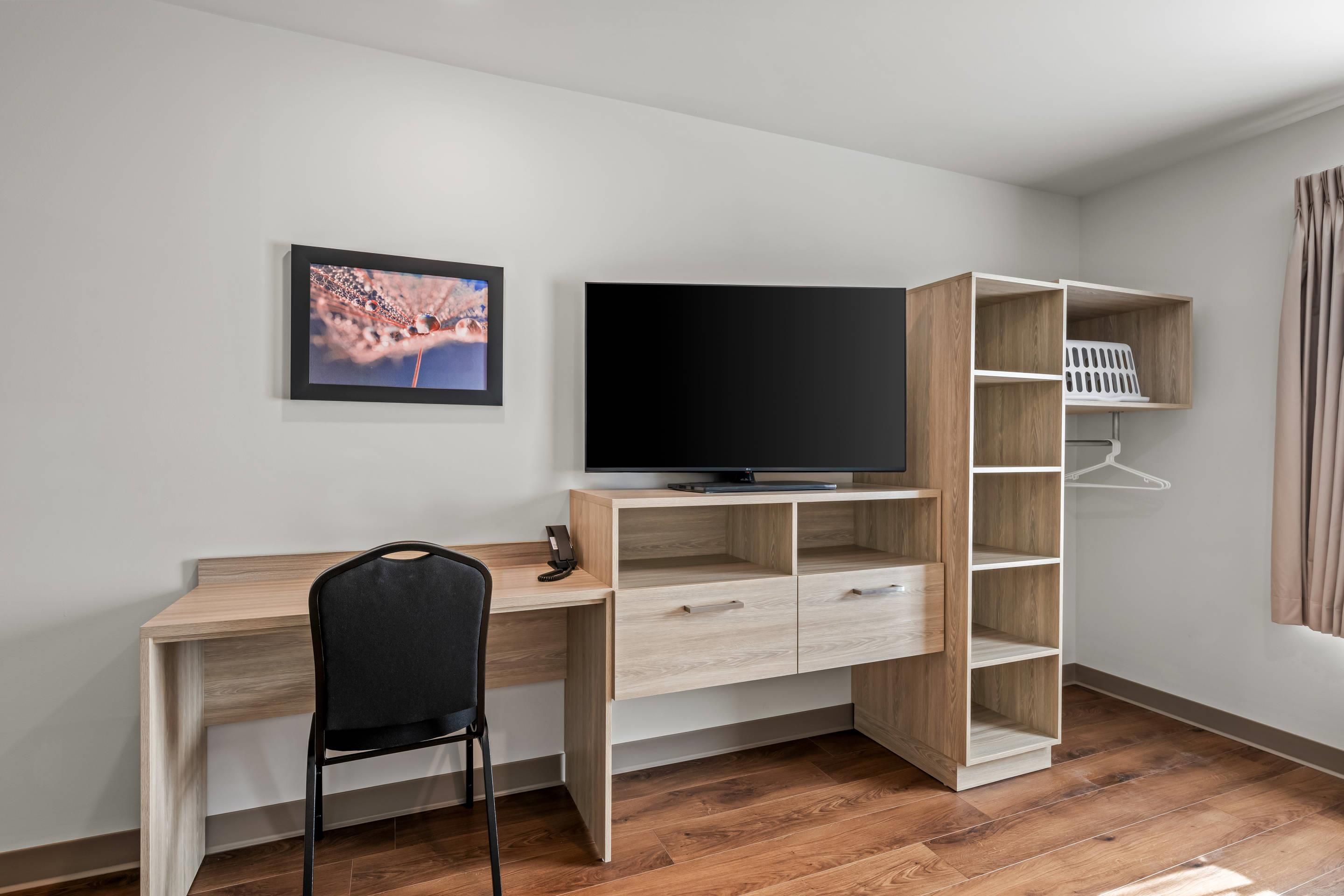Una habitación moderna con un escritorio de madera, una silla negra, un televisor de pantalla plana, un cuadro enmarcado y una estantería empotrada.