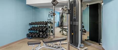 Un gimnasio en casa con una prensa de banca, mancuernas y una jaula para sentadillas.