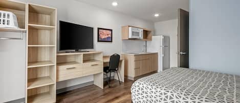 Ein kompaktes Zimmer mit Bett, Schreibtisch, Stuhl, Fernseher und einer Küchenzeile.