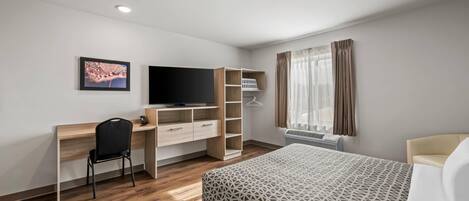 A modern hotel room with a wooden desk, a black chair, a bed with a geometric patterned bedspread, a television, and a window with curtains.