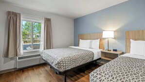 Habitación de hotel con dos camas, una ventana con cortinas, una mesita de noche con lámpara y un calefactor.