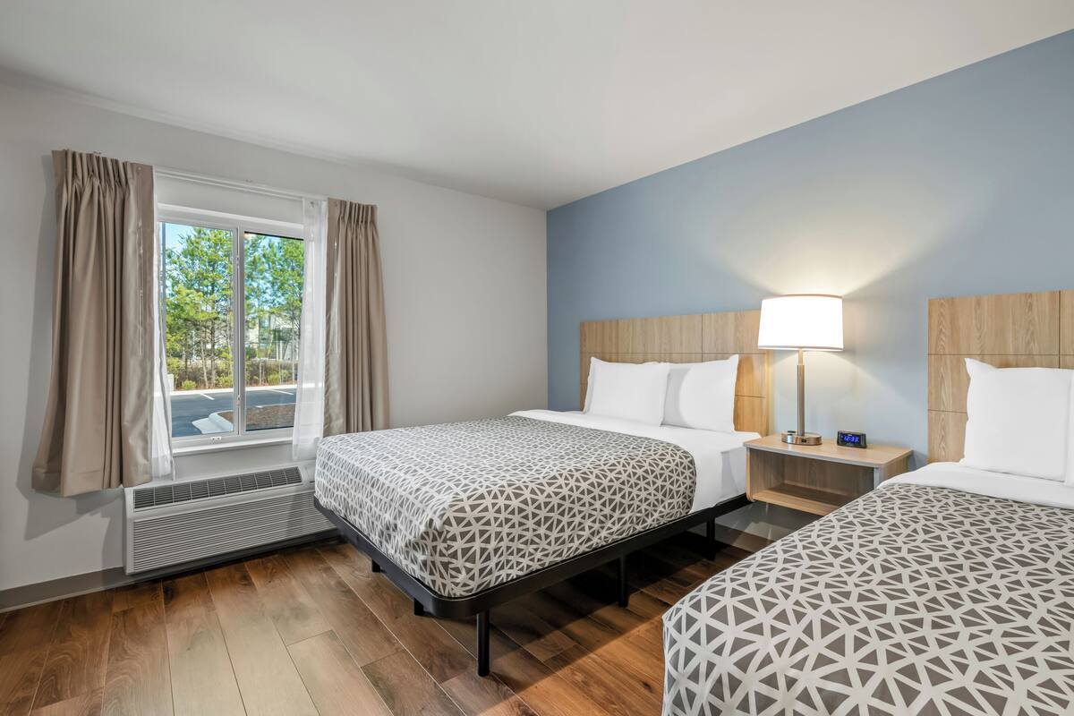 Ein Hotelzimmer mit zwei Betten, einem Fenster mit Vorhängen, einem Nachttisch mit Lampe und einem Heizgerät.