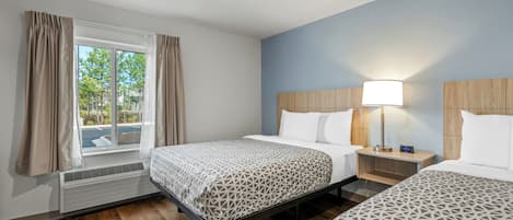 Habitación de hotel con dos camas, una ventana con cortinas, una mesita de noche con lámpara y un calefactor.