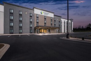 A modern hotel with a flat facade, a prominent sign, and a parking lot. - WoodSpring Suites Charlotte Northlake (Charlotte)