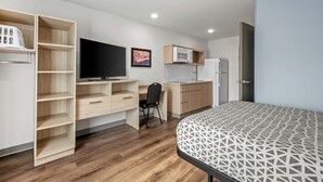 Una habitación moderna con cama, escritorio, silla, televisor, microondas y refrigerador.