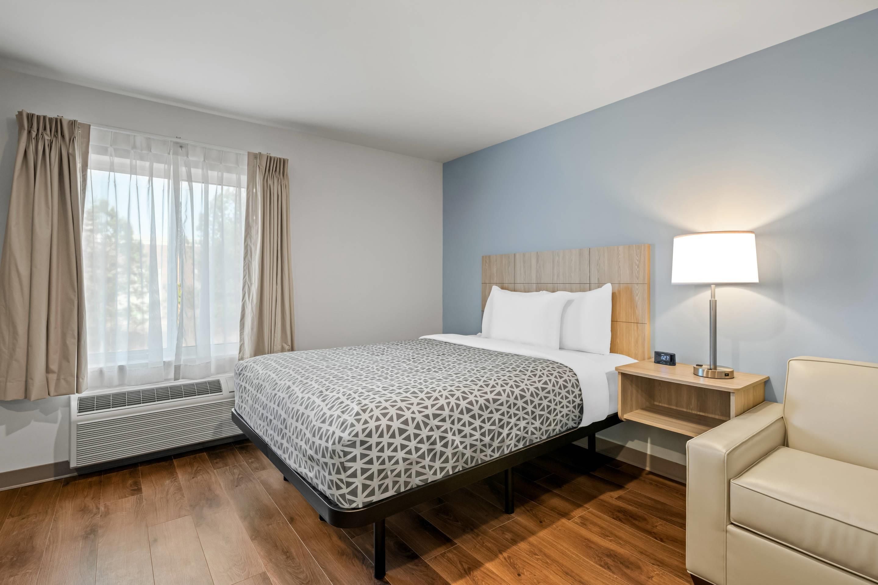 A hotel room with a bed, bedside table, lamp, and a chair.