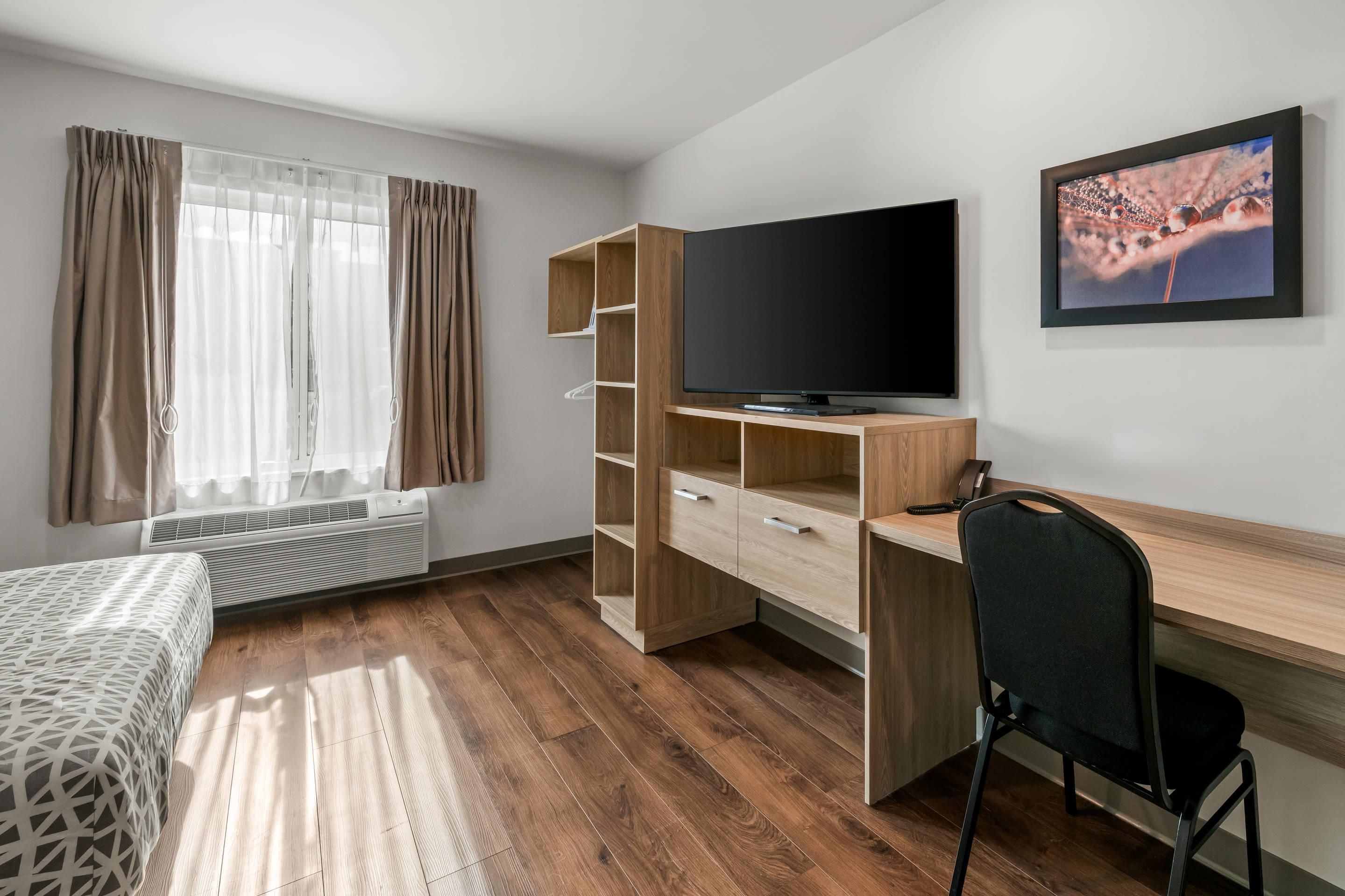 Una habitación moderna con cama, escritorio, silla, televisor y ventana con cortinas.
