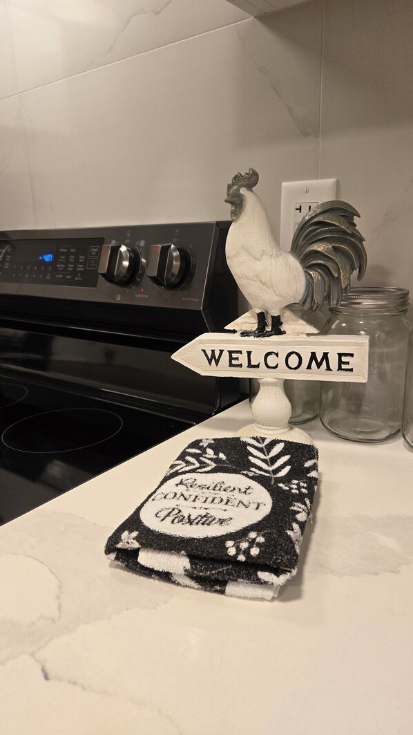 A kitchen counter with a welcome sign, a rooster decoration, and a towel with a motivational message.
