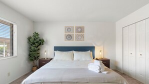 Une chambre à coucher bien rangée, avec un grand lit, une plante en pot et une table de chevet sur laquelle se trouve une lampe.