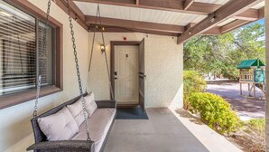 Un porche abrité avec une chaise suspendue, une porte marquée du signe « B », et une construction à toit végétalisé en arrière-plan.