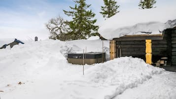 A snow-covered outdoor area with a wooden cabin, a hot tub, and a pile of firewood.