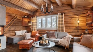 L’intérieur d’une cabane en rondins, avec une cheminée, des murs en bois, un canapé, une table basse et un lustre.