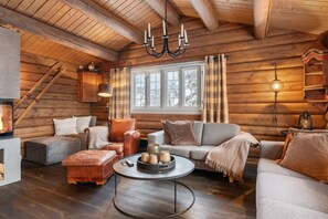 A log cabin interior with a fireplace, wooden walls, a sofa, a coffee table, and a chandelier.
