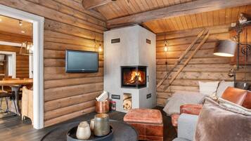 En stuga byggd av timmer med en öppen spis, en tv, en matplats och en mysig sittgrupp.