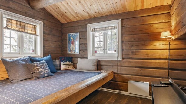 Une chambre confortable dans un chalet, avec un lit, deux fenêtres, un tableau et une lampe.