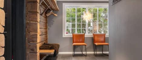 A room with a stone fireplace, two leather chairs, a window with a view, and a wall-mounted coat rack.