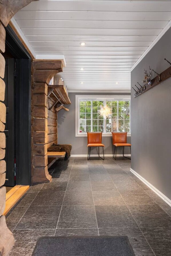 A room with a stone fireplace, two leather chairs, a window with a view, and a wall-mounted coat rack.
