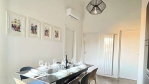 Uma sala de jantar com uma mesa comprida posta para seis pessoas, paredes brancas e uma luminária pendente moderna.