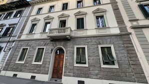 Um edifício histórico com fachada simétrica, janelas amplas e entrada central com porta de madeira.